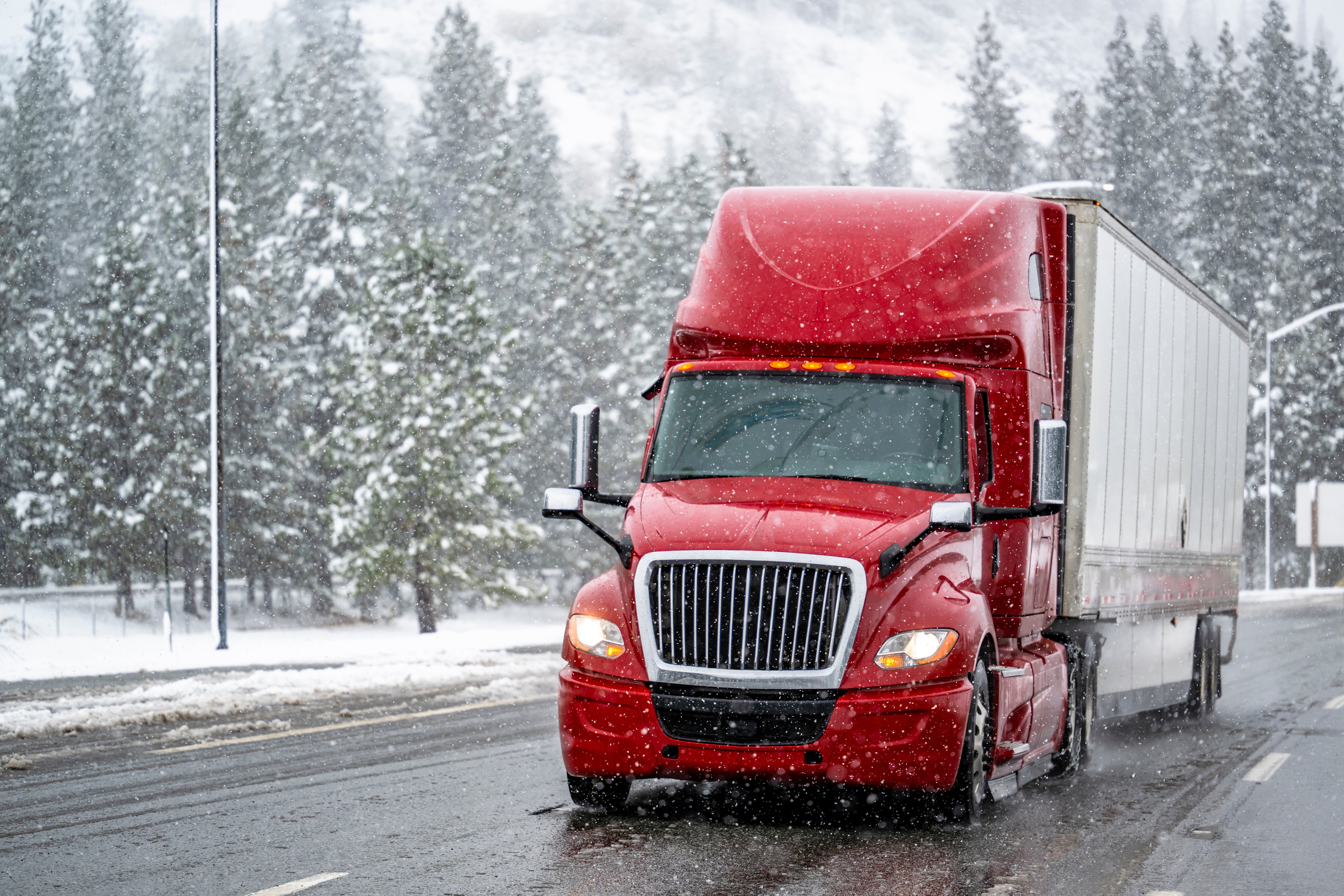 Red semi truck driving through falling snow in the winter