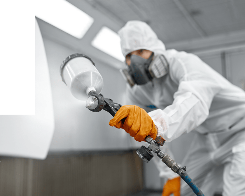 Man in PPE spraying metal parts in a booth
