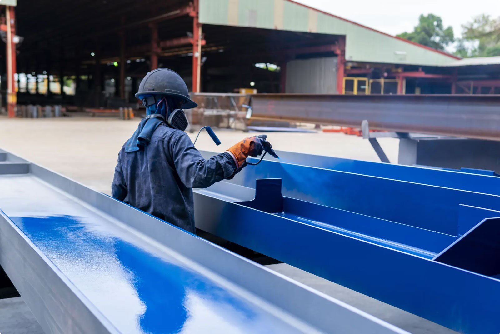Worker applying blue coating to metal beams
